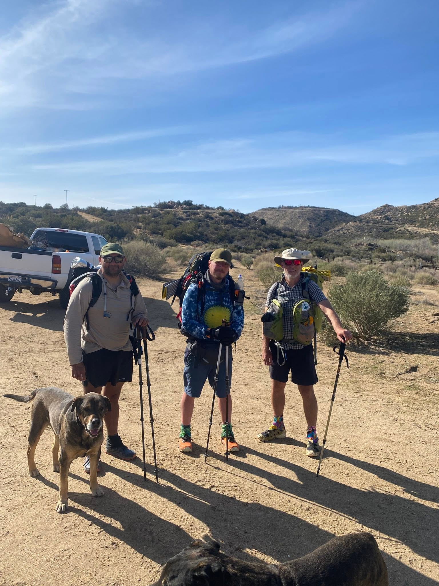 Three PCT hikers with packs and trekking poles arriving at DeBenedetti's Place