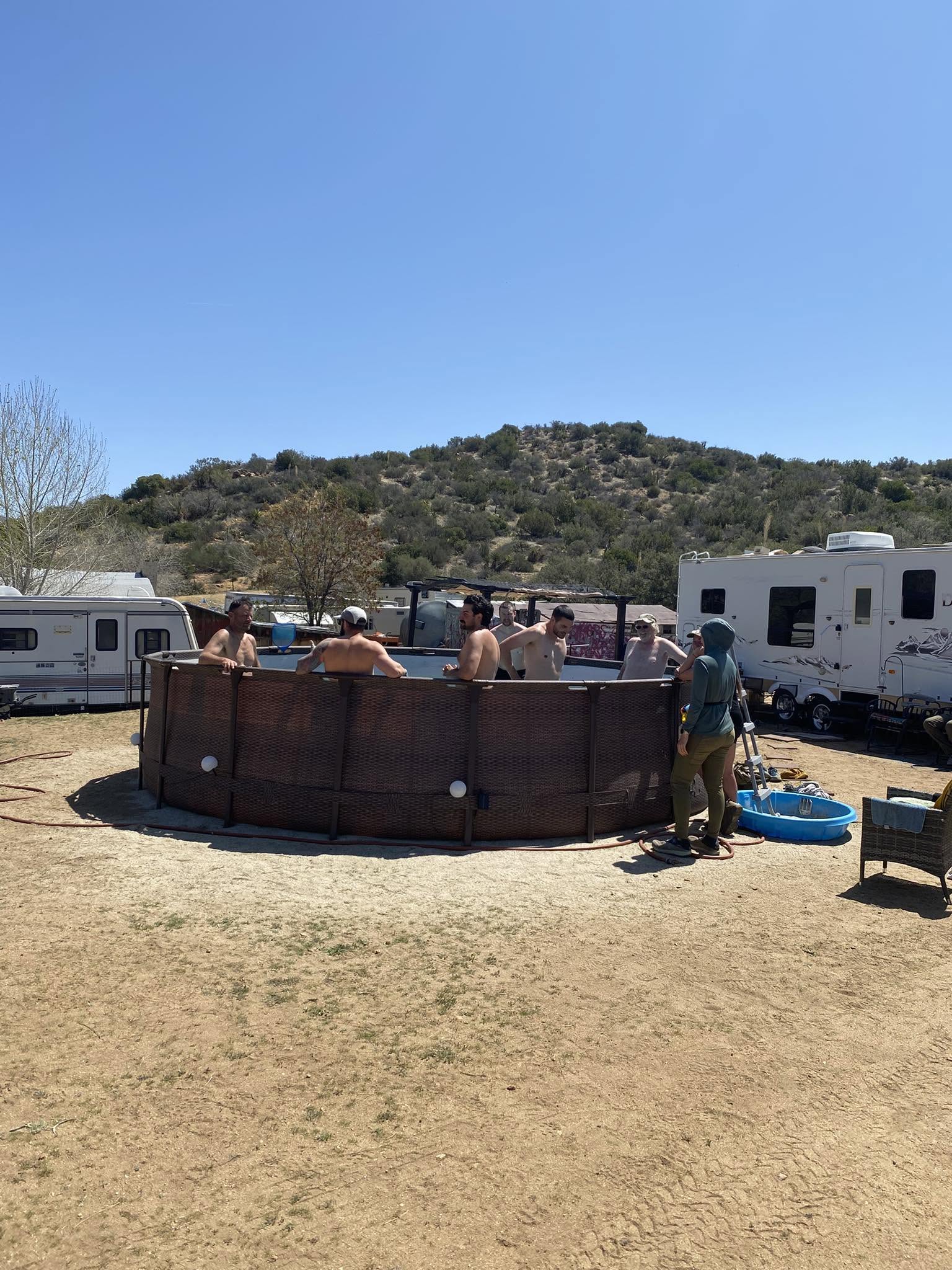 Hikers cooling off in the pool at DeBenedetti's Place with desert hills behind