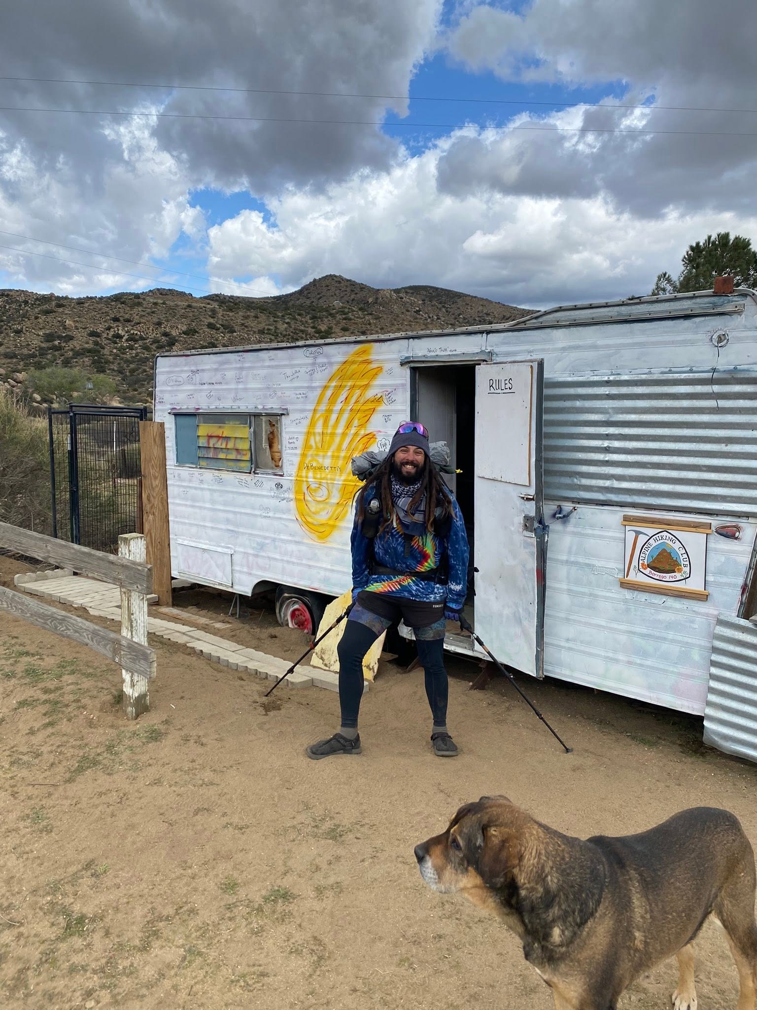 A thru-hiker in front of the signature trailer covered in hiker signatures